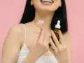 Uśmiechnięta kobieta z aparatem ortodontycznym trzyma jadeitowy roller i serum. Rozpoczyna wprowadzanie retinolu do swojej rutyny pielęgnacyjnej.