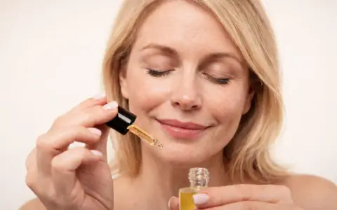 Kobieta z zamkniętymi oczami aplikuje serum z **retinolem**, dbając o skórę, by uniknąć efektów **solarium**.