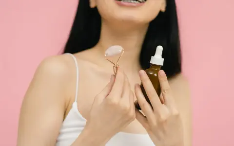 Uśmiechnięta kobieta z aparatem ortodontycznym trzyma jadeitowy roller i serum. Rozpoczyna wprowadzanie retinolu do swojej rutyny pielęgnacyjnej.